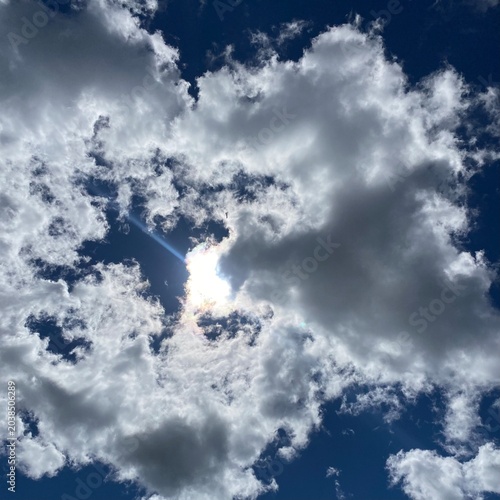 Sun shining through dramatic clouds in dark blue sky, bright sunbeam and sun flare burst breaking through cumulus cloudscape background