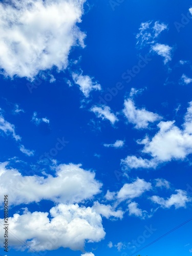Blue sky background with fluffy white cumulus clouds on a bright sunny day, clear weather vertical sky scape for graphic design copy space