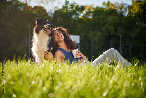 Принти на полотні Young woman with curly hair sits in green grass, enjoying a sunny day outdoors w