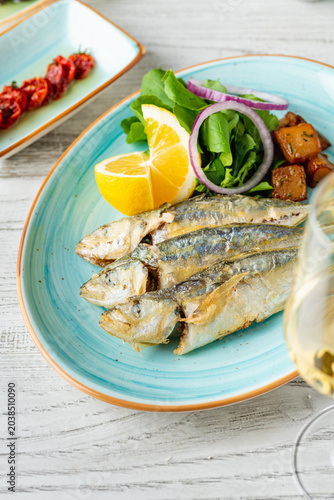 Grilled horse mackerel served with lemon, onion and greens in Mediterranean style presentation