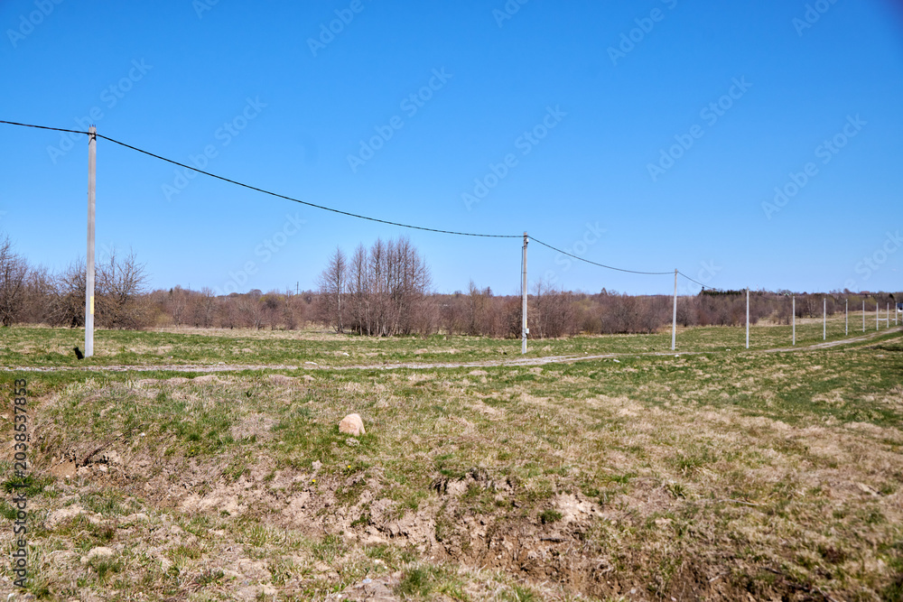 Fototapeta premium Rural landscape with electrical poles extending through grassy field under clear blue sky