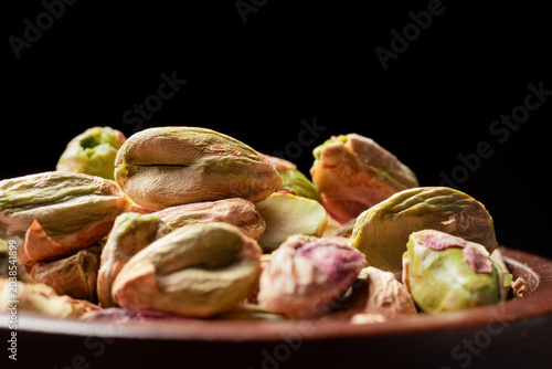 Pile of roasted shelled pistachio kernels in brown wooden bowl on black  backbackground