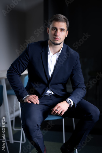 Принти на полотні Male business professional in a dark suit seated on a chair, showcasing a confid