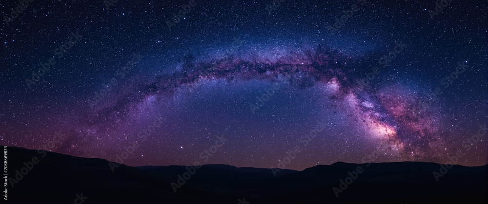 Obraz premium Expansive space background capturing purple Milky Way and stars over gentle hills at summer night