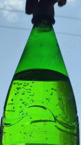 A hand unscrews the cap of a bottle of sparkling water. Woman opens a bottle of soda and drops sprayed