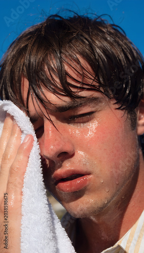 portrait of Young man wiping sweat with a towel under intense scorching sun. 
