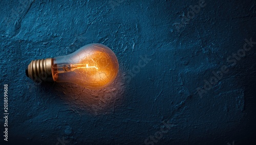 Cracked bulb glowing brightly on rough textured blue surface with copy space