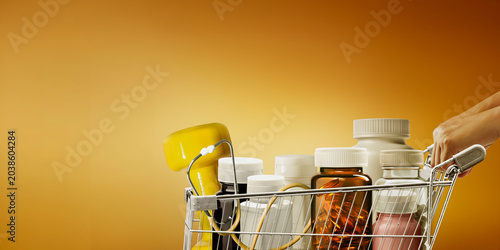 Foto A shopping cart is filled with bottles of dietary supplements to address malnutrition and dietary supplement businesses promoting balanced diets, all against a yellow background