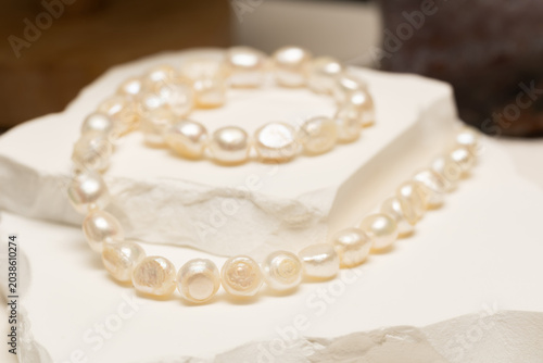 A bracelet and necklace made from natural stone pearls sit on a display surface. They are arranged neatly around a white stone. Customers can admire the jewelry.