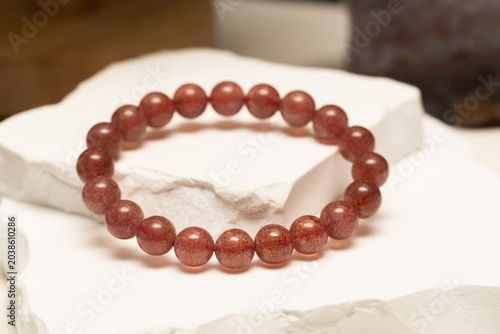 A strawberry quartz bracelet sits on a stone surface. The bracelet has round beads and showcases a warm color. The display highlights its natural beauty and shine.