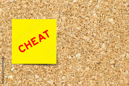 Yellow note paper with word cheat on cork board background with copy space