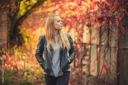 Thoughtful blonde woman in leather jacket outdoors during autumn