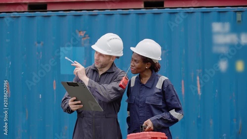 Diverse Two Logistics Workers in Hard Hats Inspecting Shipping Stacked Containers in Container Yard
