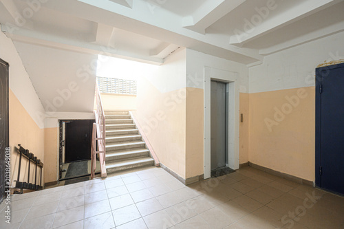 communal hallway with beige walls, tiled flooring, a central staircase with wooden railings, an elevator door, and a dark entrance door under a skylight