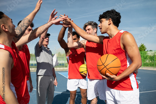 Basketball team and coach forming a huddle, hands together for teamwork