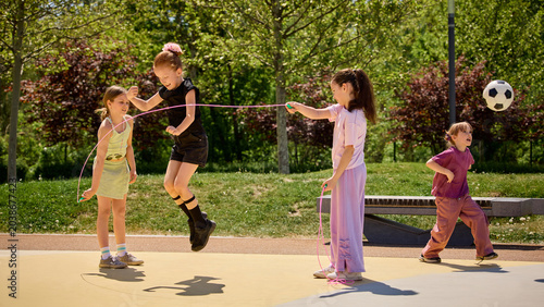 Bild auf Leinwand Children jumping rope and playing with ball outdoors in bright summer park