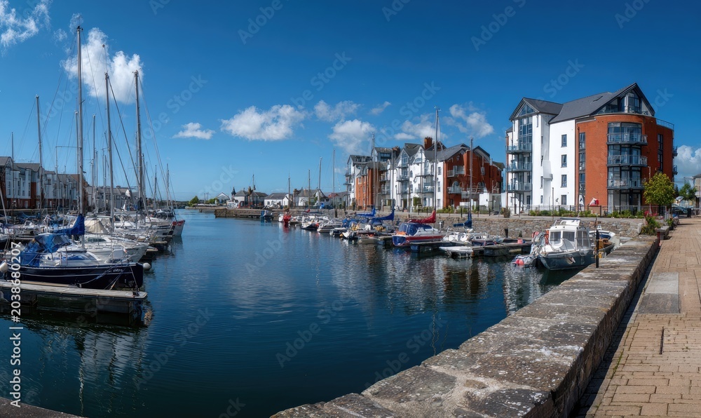 Fototapeta premium Modern waterfront buildings with sailboats moored in a harbor under blue sky