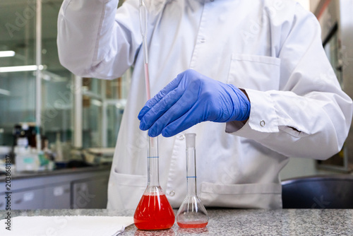 Obraz na płótnie Scientist hands in gloves using pipette with red liquid in volumetric flask in p