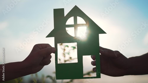 Family mortgage concept. Family holds paper house with their hands at sunset. Family house on loan. Paper house is symbol of family happiness.Housing and mortgage crisis.Dream concept of buying house