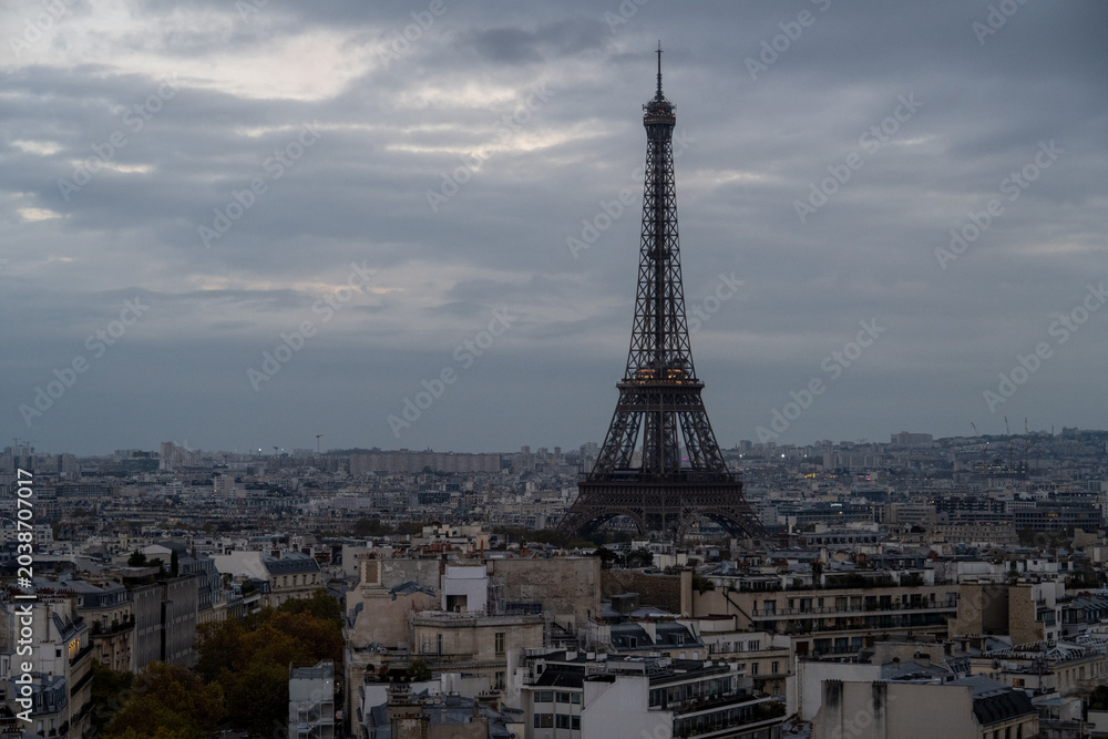 Fototapeta premium Eiffel Tower over Paris rooftops under cloudy sky