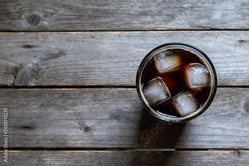 Glass of iced cola on rustic wooden table top view