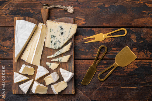 Photography Assorted soft and blue cheeses on a rustic wooden board set over a dark weathered background for a warm artisan food style