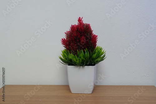 Small artificial red and green plant in a white plastic pot on a wooden table