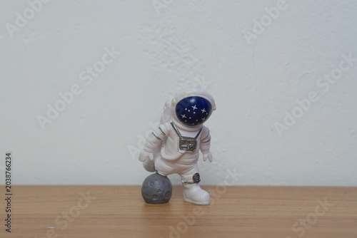 Cute miniature astronaut figurine stepping on a small gray cratered moon on a wooden table