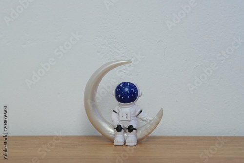 Cute miniature astronaut figurine sitting on a white crescent moon on a wooden table