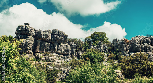 Eroded grey steep rock formations with some vegetation under a blue sky with some clouds. National Park of El Torcal de Antequera, Andalusia, Spain.