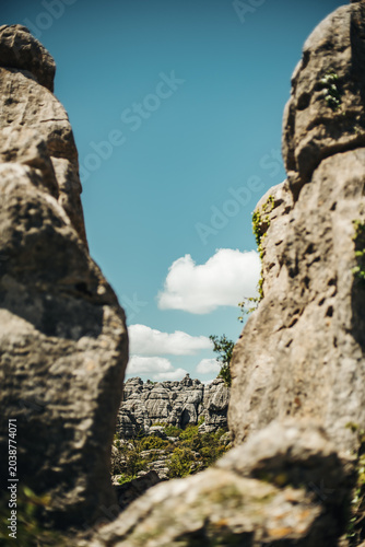 Eroded grey steep rock formations with some vegetation under a blue sky with some clouds. National Park of El Torcal de Antequera, Andalusia, Spain.