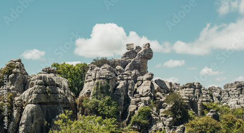 Eroded grey steep rock formations with some vegetation under a blue sky with some clouds. National Park of El Torcal de Antequera, Andalusia, Spain.