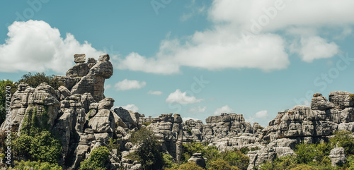 Eroded grey steep rock formations with some vegetation under a blue sky with some clouds. National Park of El Torcal de Antequera, Andalusia, Spain.