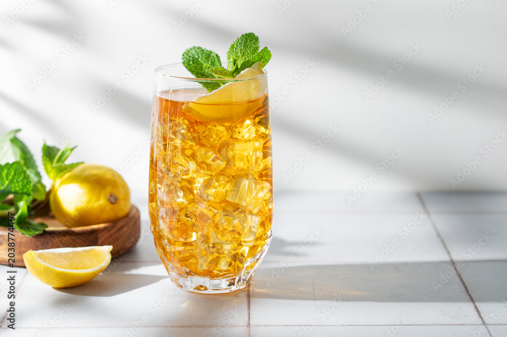Fototapeta premium Iced tea with lemon and mint in a glass on a light tile background with shadows