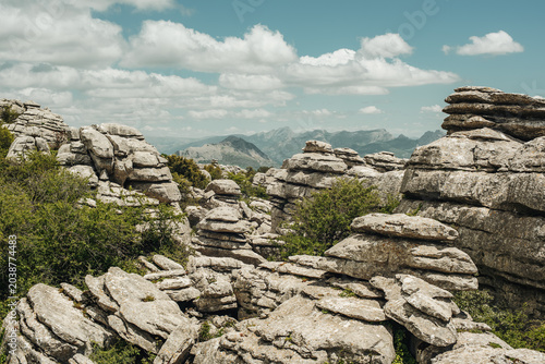 Eroded grey steep rock formations with some vegetation under a blue sky with some clouds. National Park of El Torcal de Antequera, Andalusia, Spain.