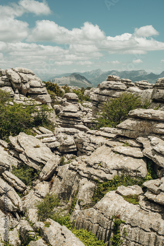 Eroded grey steep rock formations with some vegetation under a blue sky with some clouds. National Park of El Torcal de Antequera, Andalusia, Spain.