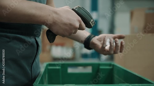 Warehouse worker using a handheld barcode scanner to process items in a green plastic crate, performing inventory tracking and order picking tasks in a logistics environment