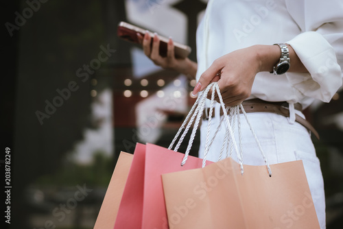Tableau sur toile Close-up of a shopper carrying colorful shopping bags outdoors, symbolizing retail spending, consumer lifestyle, fashion purchases, and modern shopping experiences