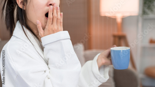 Tableau sur toile Asian young women yawning holding coffee mug wearing white bathrobe during morni