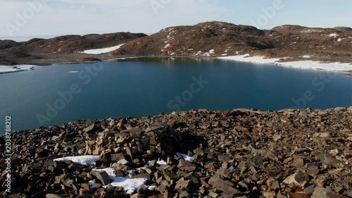 Antarctic scenery featuring an oasis with small lakes and calm water surfaces beneath a clear blue sky.