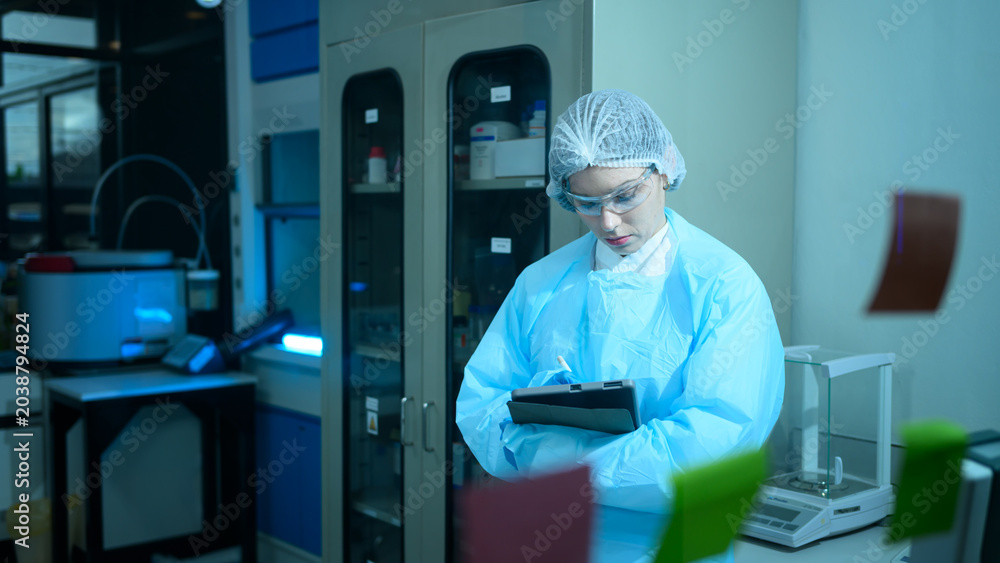 Naklejka premium Female Lab Technician in Protective Gear Using Tablet in Modern Scientific Laboratory