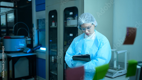 Female Lab Technician in Protective Gear Using Tablet in Modern Scientific Laboratory