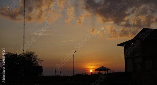 sunset, a bright afternoon sky with orange and black clouds indicating that evening is coming, and the silhouette of a building