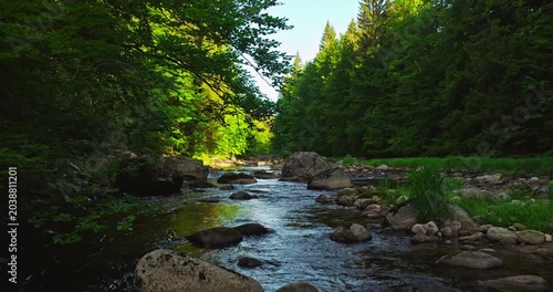 Gentle flyover above a rocky mountain river during spring sunrise with realistic ambient sounds of river and birds. Peaceful flowing water surrounded by green forest landscape with morning light. 