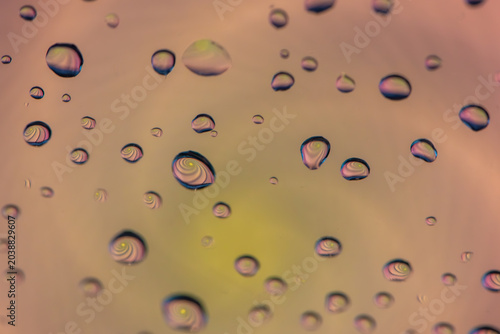 An abstract arrangement of water droplets on a surface, reflecting iridescent colors and abstract patterns within their curved forms against a soft, gradient background