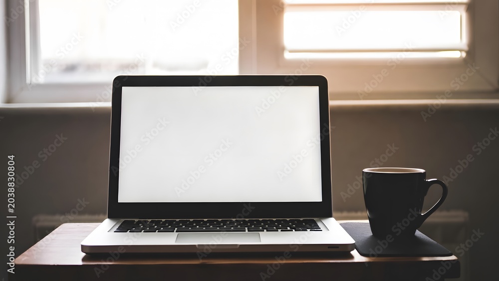 Fototapeta premium aptop with Blank White Screen and Coffee Cup on Wooden Desk for Digital Marketing Mockup. Professional workspace featuring a modern laptop with a blank white screen positioned on a wooden 