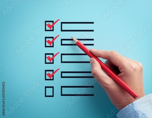 hand checking off items on a checklist with a red pencil against a light blue background
