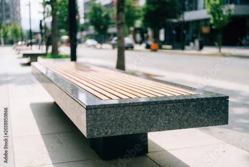 Modern Urban Concrete and Wood Bench on City Sidewalk With Blurred Background and Cars