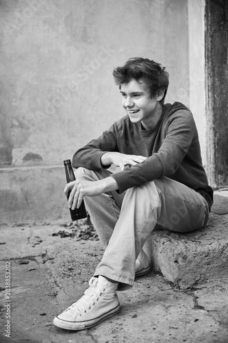 Canvas Print Teenage male holds bottle while sitting outside building entrance