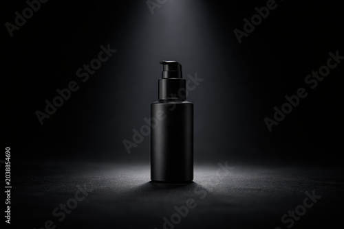 Matte black pump bottle on dramatic spotlighted dark background for cosmetic packaging mockup and luxury branding design